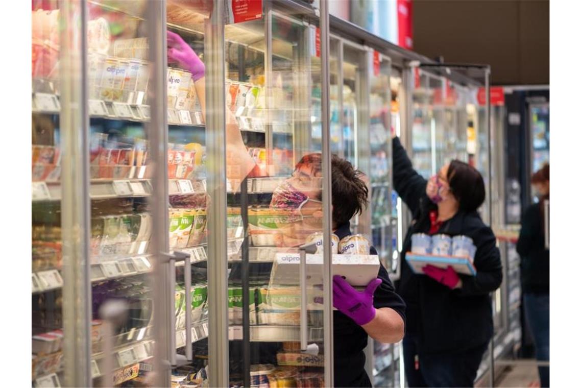 Mitarbeiterinnen in einem Supermarkt tragen Schutzmasken, während sie die Kühlregale mit Waren bestücken. Foto: Robert Michael/dpa-Zentralbild/dpa