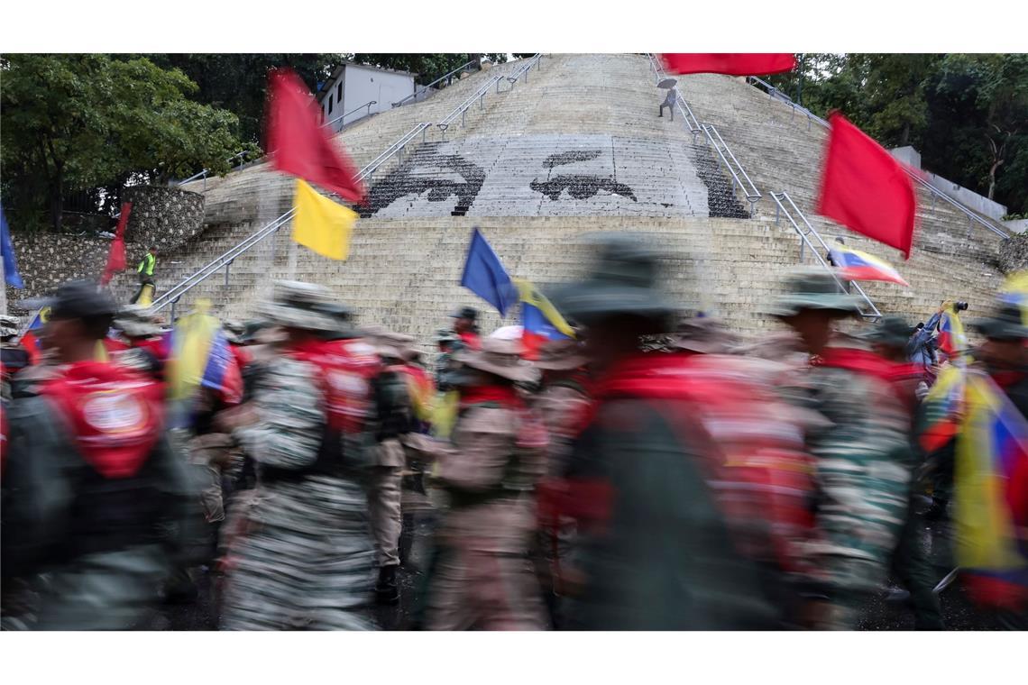 Mitglieder der Bolivarischen Miliz marschieren vor einer Treppe in Caracas, auf der die Augen des verstorbenen Präsidenten Hugo Chavez abgebildet sind, während einer Demonstration zum Gedenken an den Jahrestag der Schlacht von Santa Ines, die während des venezolanischen Bundeskriegs im 19. Jahrhundert stattfand.