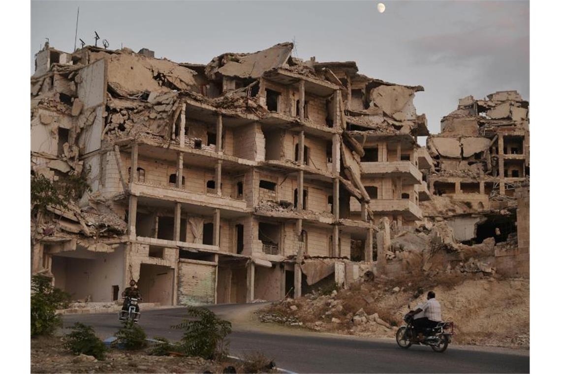 Motorradfahrer passieren zerstörte Gebäude in der Provinz Idlib. Das Auswärtige Amt schätzt nicht nur die Region um Idlib, sondern ganz Syrien als gefährlich für Rückkehrer ein. Foto: Ugur Can/DHA via AP/dpa