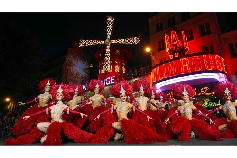 Moulin Rouge-Tänzerinnen und -Tänzer agieren vor den neuen Flügel der Windmühle des Moulin Rouge, die sich drehen, während das Kabarett in Paris seine Wiederinbetriebnahme feiert. Vierzehn Monate nach ihrem Sturz wurden die Flügel des Moulin Rouge wieder installiert und drehen sich nun wieder, womit eine mehr als 135 Jahre alte Tradition wiederbelebt wird.
