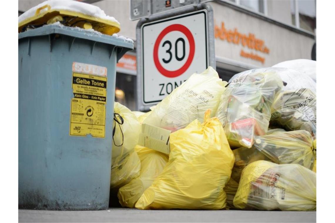 Mülltonnen und gelbe Säcke mit Kunststoff-Abfällen stapeln sich auf einem Fußweg. Foto: Sina Schuldt/dpa