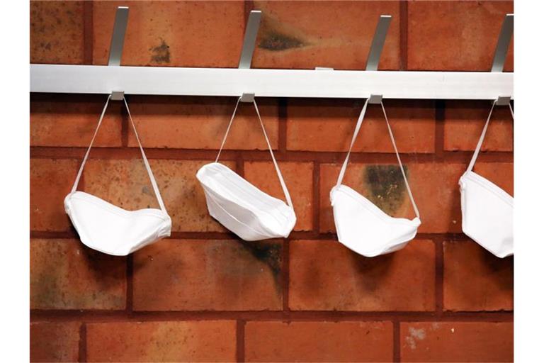 Mund-Nase-Schutzmasken hängen an Haken. Foto: Rene Traut/dpa/Symbolbild