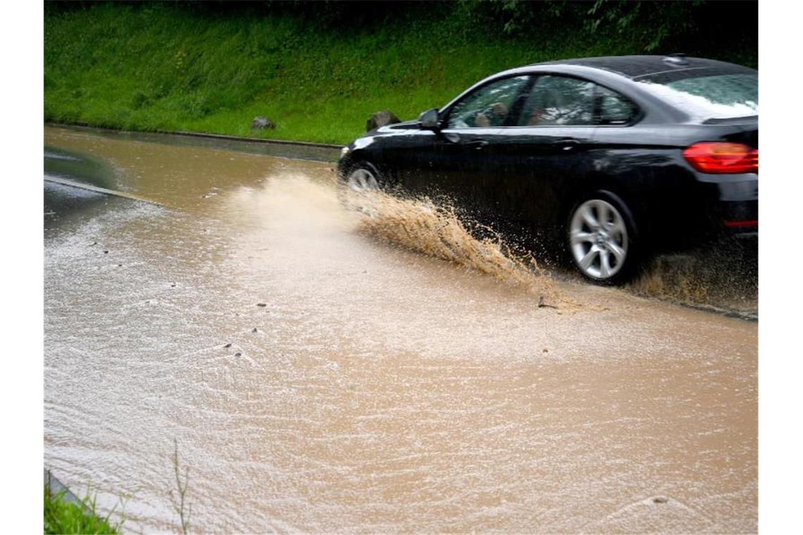 Nach einem Gewitterregen fährt ein Auto auf einer Landstraße durch eine große Wasserpfütze. Foto: Rene Priebe/dpa/Symbolbild