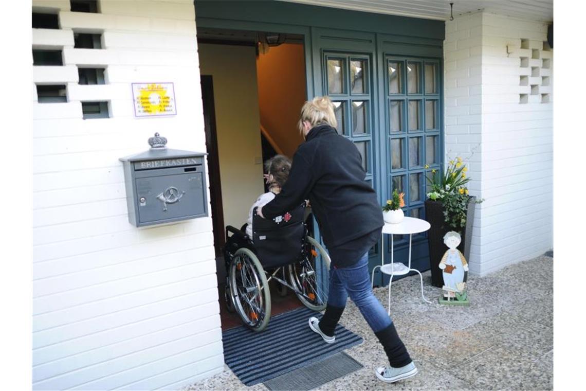 Nach einem kurzen Ausflug schiebt eine Altenpflegerin eine Bewohnerin mit Rollstuhl in die Pflege-WG. Foto: Christian Charisius/Archivbild