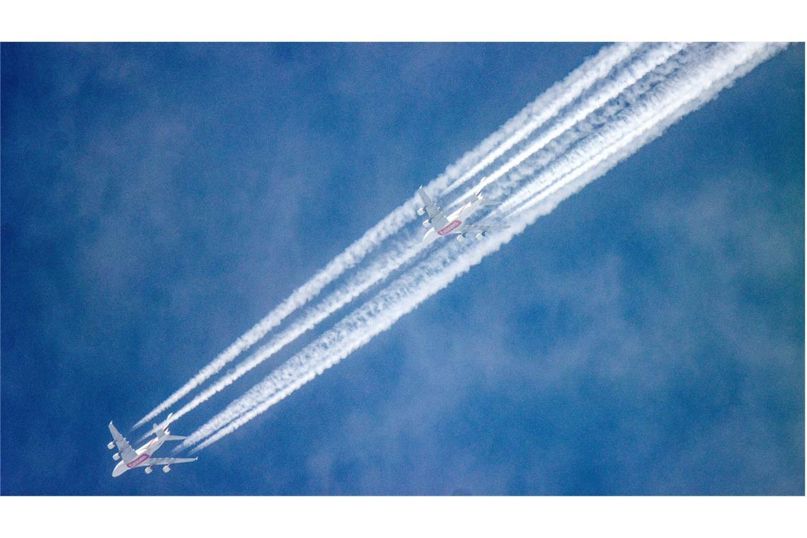 Wie Kondensstreifen dem Klima massiv schaden Neben dem abnehmenden Mond hinterlassen zwei Passagierflugzeuge am blauen Himmel Kondensstreifen.