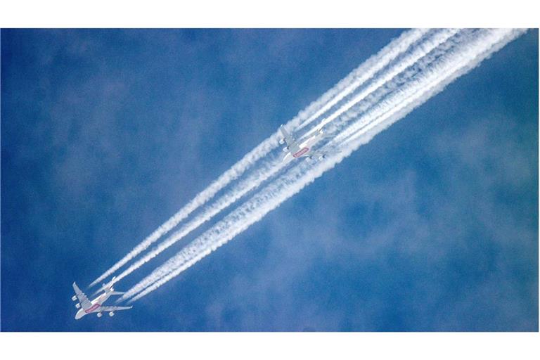 Neben dem abnehmenden Mond hinterlassen zwei Passagierflugzeuge am blauen Himmel Kondensstreifen.