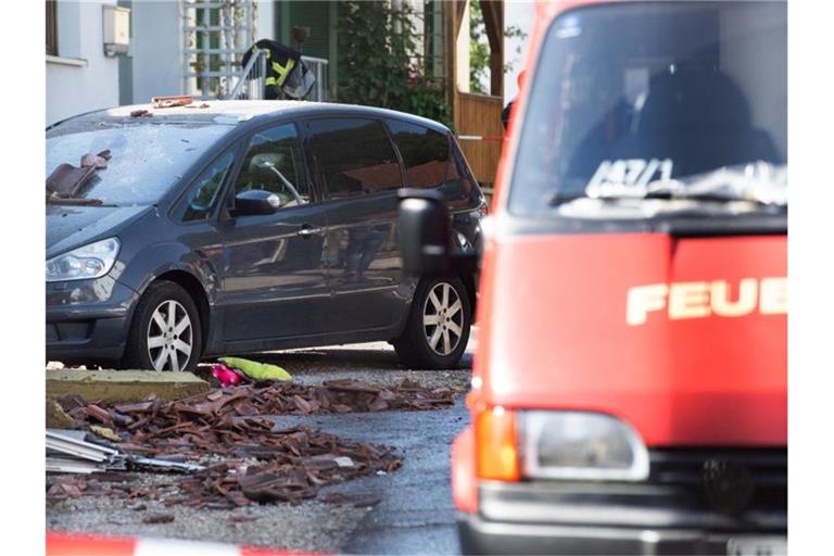 Neben einem Feuerwehrfahrzeug steht ein Auto vor einem stark beschädigten Haus, an und auf dem Auto liegen Trümmer. Foto: Stefan Puchner