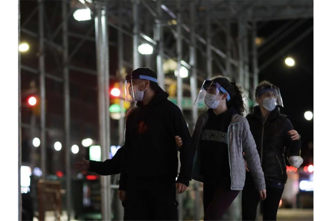 Corona-Pandemie: Mehr als 10.000 Todesfälle in New York New Yorker gehen mit Mundschutz und Gesichtsmaske eine Straße entlang. Foto: Mark Lennihan/AP/dpa