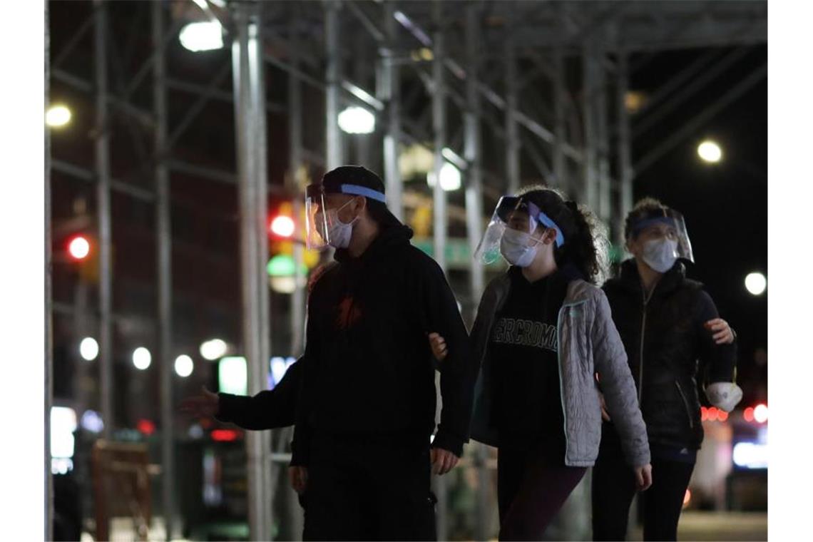 New Yorker gehen mit Mundschutz und Gesichtsmaske eine Straße entlang. Foto: Mark Lennihan/AP/dpa