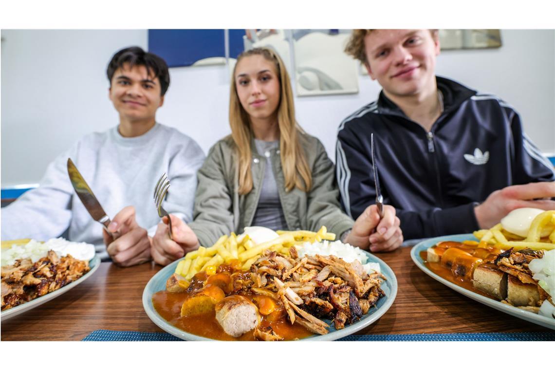 Nickolas Krugmann (li.-re.), Antonija Dreznjak und Lukas Kampen sitzen vor ihren „Taxi-Tellern“ in einem Imbiss. Pommes, Currywurst und dazu massenweise Gyros mit Zwiebeln: Im Ruhrgebiet sorgt der Taxi-Teller für Begeisterung bei Fast-Food-Fans. Das Gericht ist länger bekannt, neuerdings aber voll im Trend.