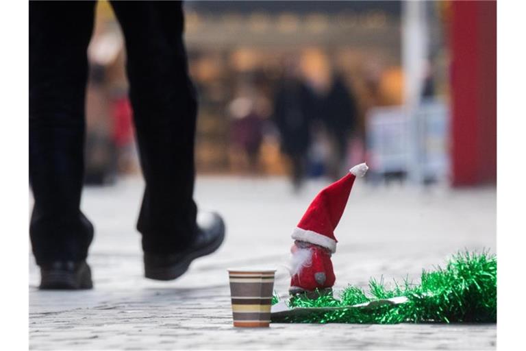 Obdachlose bitten mit einem Pappbecher und einem kleinen Weihnachtsmann um Spenden. Foto: Julian Stratenschulte/dpa/Symbolbild