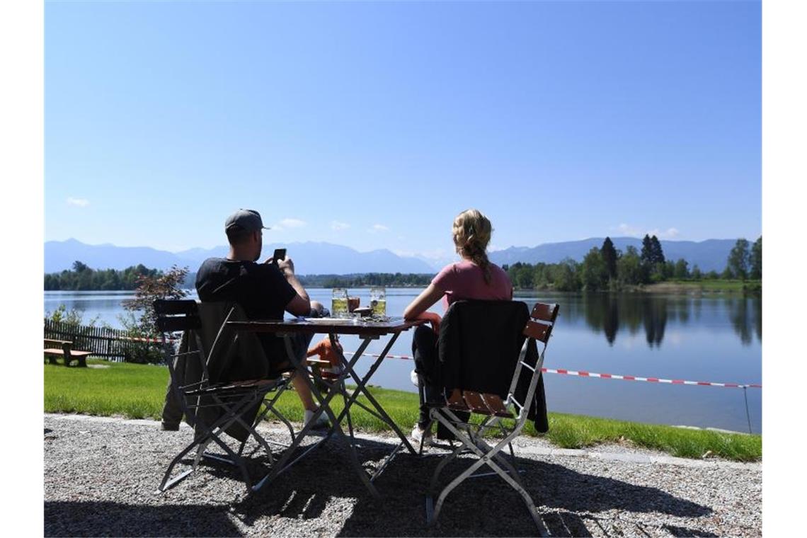 Pärchen genießt ein Bier in der Sonne in einem Biergarten am See. Foto: Angelika Warmuth/dpa