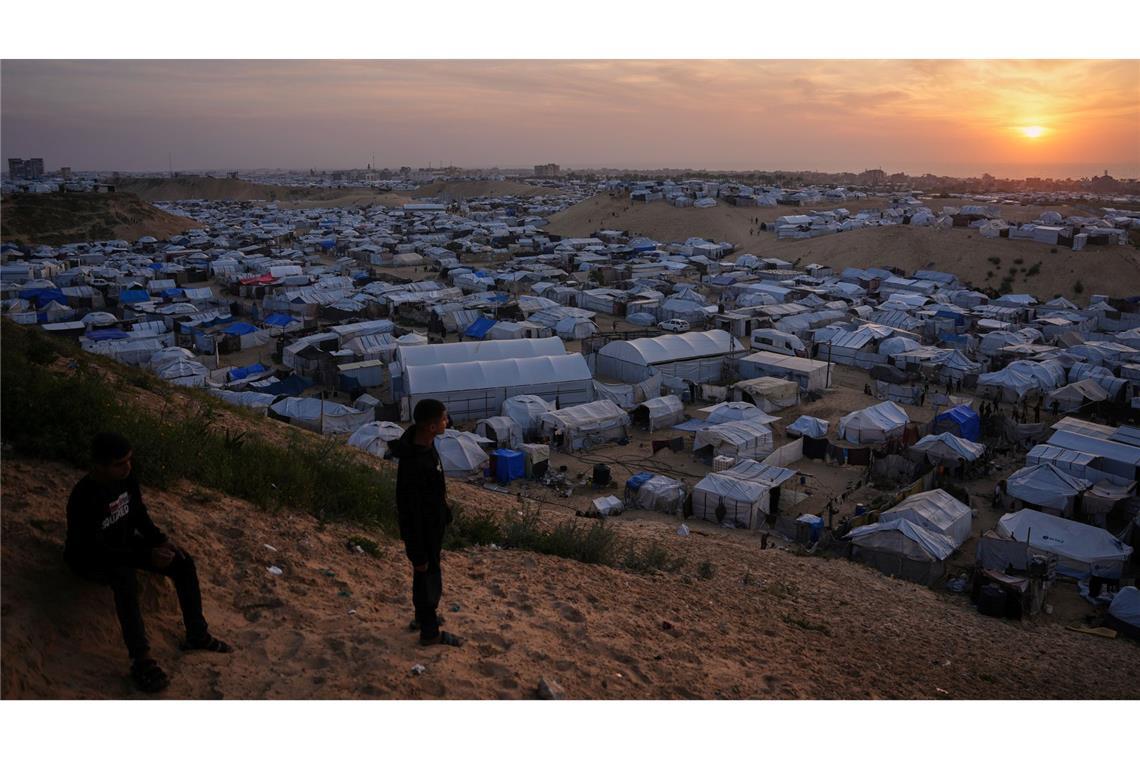 Palästinensische Jugendliche schauen im südlichen Gazastreifen dem Sonnenuntergang zu, als sie in einem behelfsmäßigen Lager für Vertriebene vor Zelten stehen.