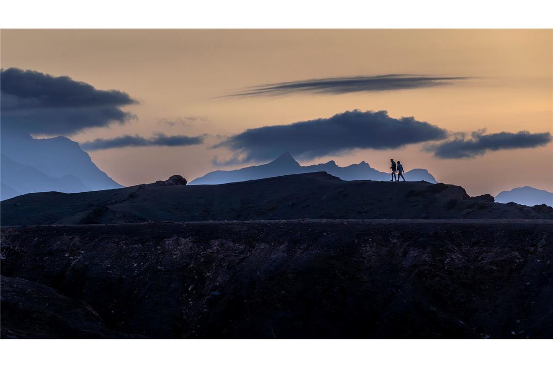 Panodrama: Menschen gehen auf der Insel Fuerteventura unter dramatisch wirkenden Wolkenformationen.
