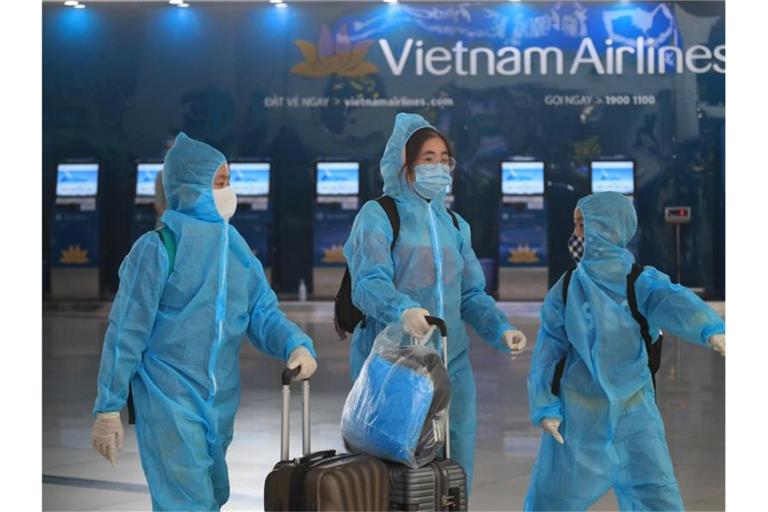 Passagiere in voller Schutzkleidung gegen das Coronavirus gehen durch den Flughafen Hanoi. Foto: Hau Dinh/AP/dpa