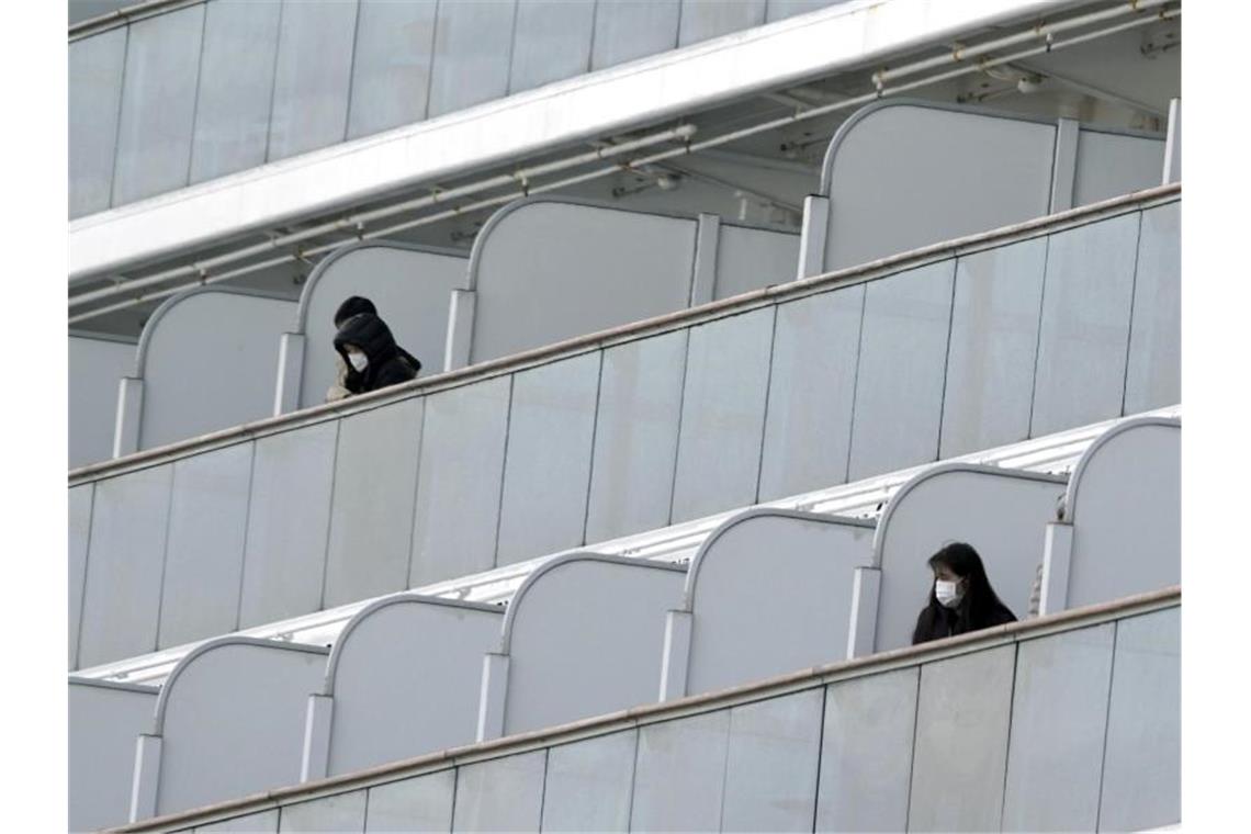 Passagiere mit Mundschutz auf Balkonen des Kreuzfahrtschiffs „Diamond Princess“ im Hafen von Yokohama. Foto: Eugene Hoshiko/AP/dpa