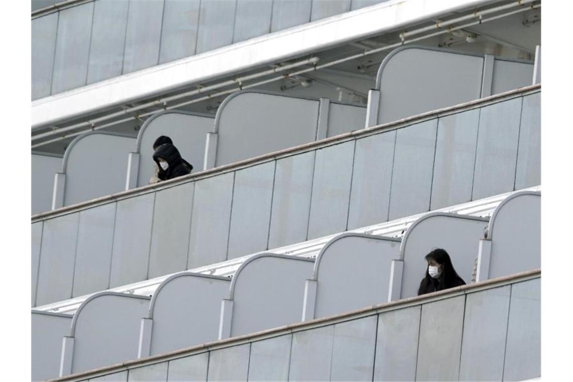 Passagiere mit Mundschutz auf Balkonen des Kreuzfahrtschiffs „Diamond Princess“ im Hafen von Yokohama. Foto: Eugene Hoshiko/AP/dpa