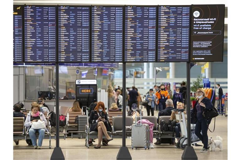 Passagiere sitzen auf dem internationalen Flughafen Scheremetjewo in Moskau unter einer Fluginformationstafel. Russland nimmt trotz der Corona-Pandemie den regulären Flugverkehr mit acht Ländern wieder auf. Foto: Alexander Zemlianichenko Jr/XinHua/dpa