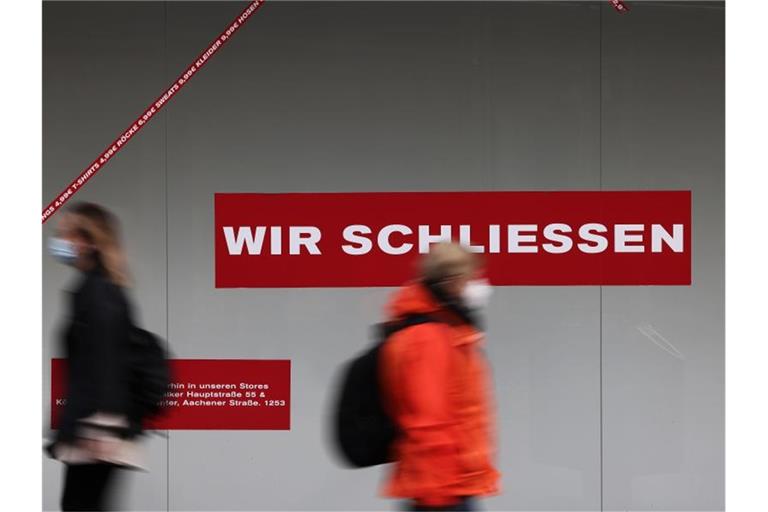 Passanten gehen in der Kölner Innenstadt an einem geschlossen Ladenlokal vorbei. Foto: Oliver Berg/dpa