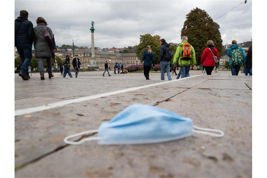 Passanten gehen über den Schlossplatz, während auf dem Boden eine Mund-Nasen-Bedeckung liegt. Foto: Tom Weller/dpa