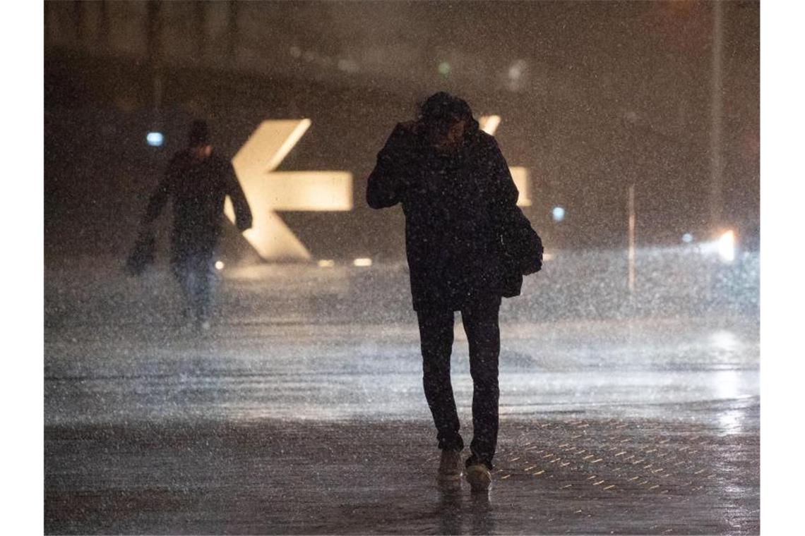 Passanten kämpfen sich durch strömenden Regen. Foto: Marijan Murat/dpa