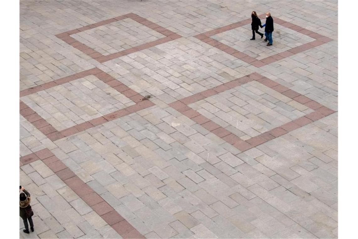 Passanten laufen über den fast leeren Marienplatz vor dem Rathaus in der Innenstadt von München. Foto: Peter Kneffel/dpa