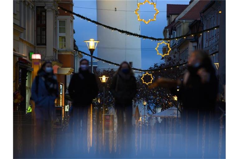 Passanten mit Mund-Nasen-Schutz gehen durch eine festlich dekorierte Fußgängerzone. Foto: Robert Michael/dpa-Zentralbild/dpa/Symbolbild