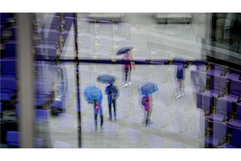Passanten mit Regenschirmen spiegeln sich in den Fenstern vor dem Plenarsaal des Bundestags.
