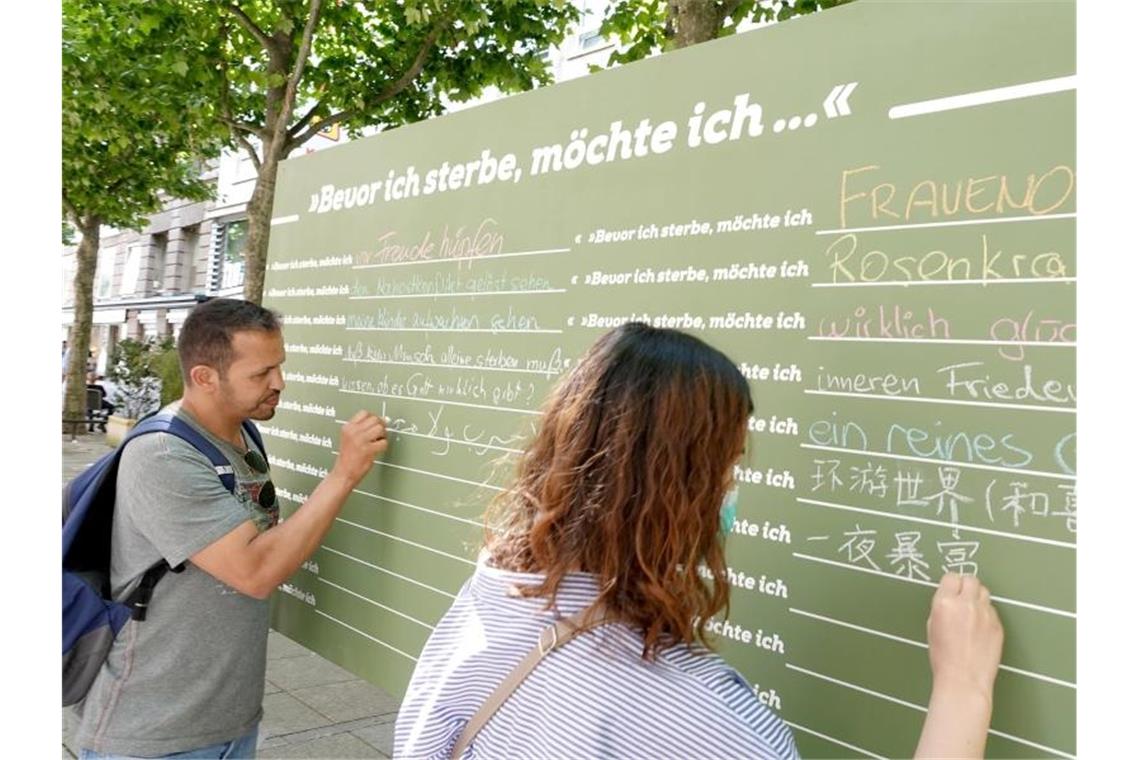 Passanten schreiben auf eine Tafel, was sie machen möchten, bevor sie sterben. Foto: Felix Schröder/dpa