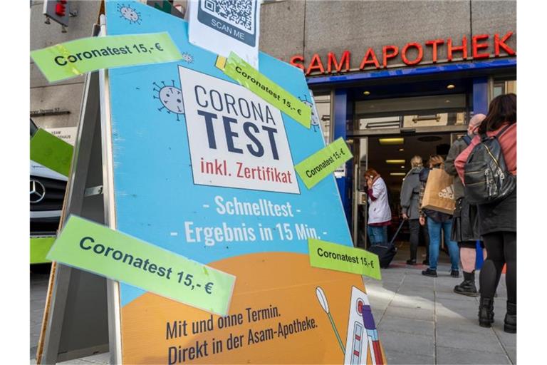 Passanten stehen in der Münchner Innenstadt vor einer Apotheke, die Coronatest für 15 Euro anbietet. Foto: Peter Kneffel/dpa