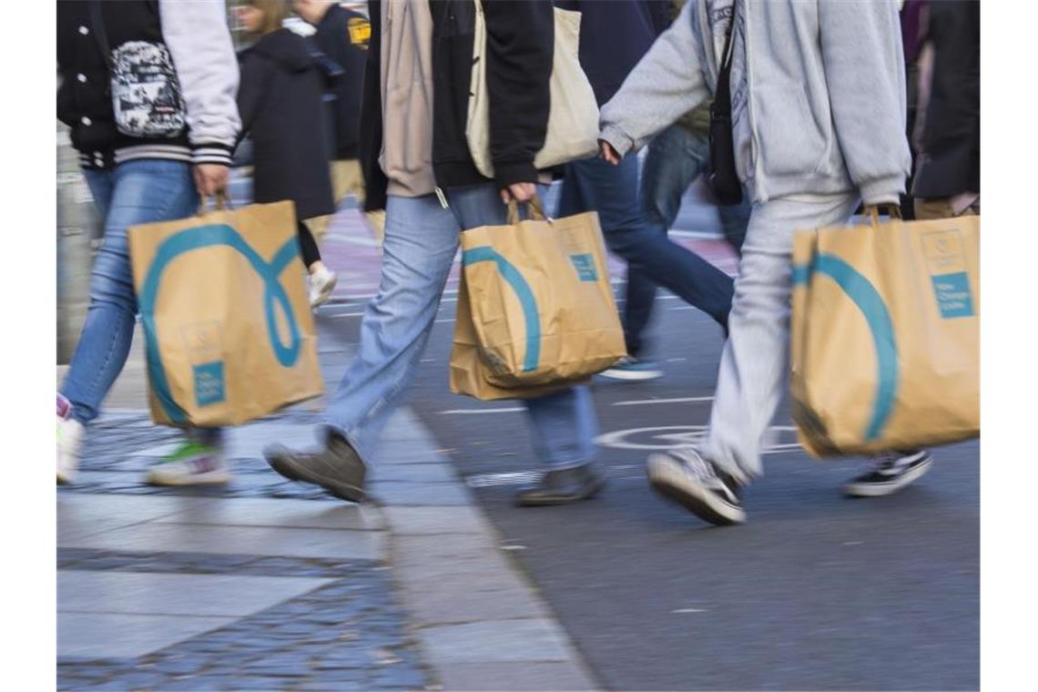 Passanten tragen Einkaufstaschen beim Überqueren einer Straße. Foto: Carsten Koall/dpa/Symbolbild