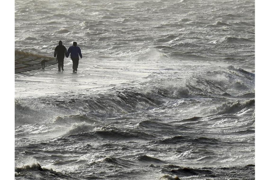 Passanten trotzen am Nordseedeich dem Sturm. Foto: Carsten Rehder/dpa