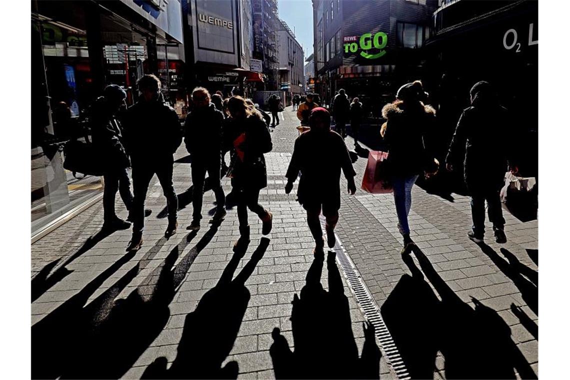 Passanten werfen in einer Kölner Fußgängerzone lange Schatten. Foto: Oliver Berg/dpa