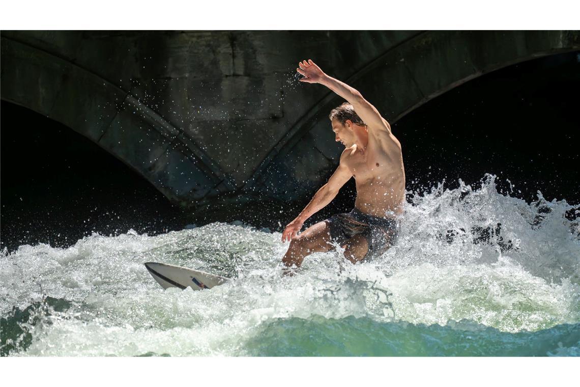 Patrick surft bei sommerlichen Temperaturen mit seinem Board auf der Eisbachwelle im Englischen Garten in München.