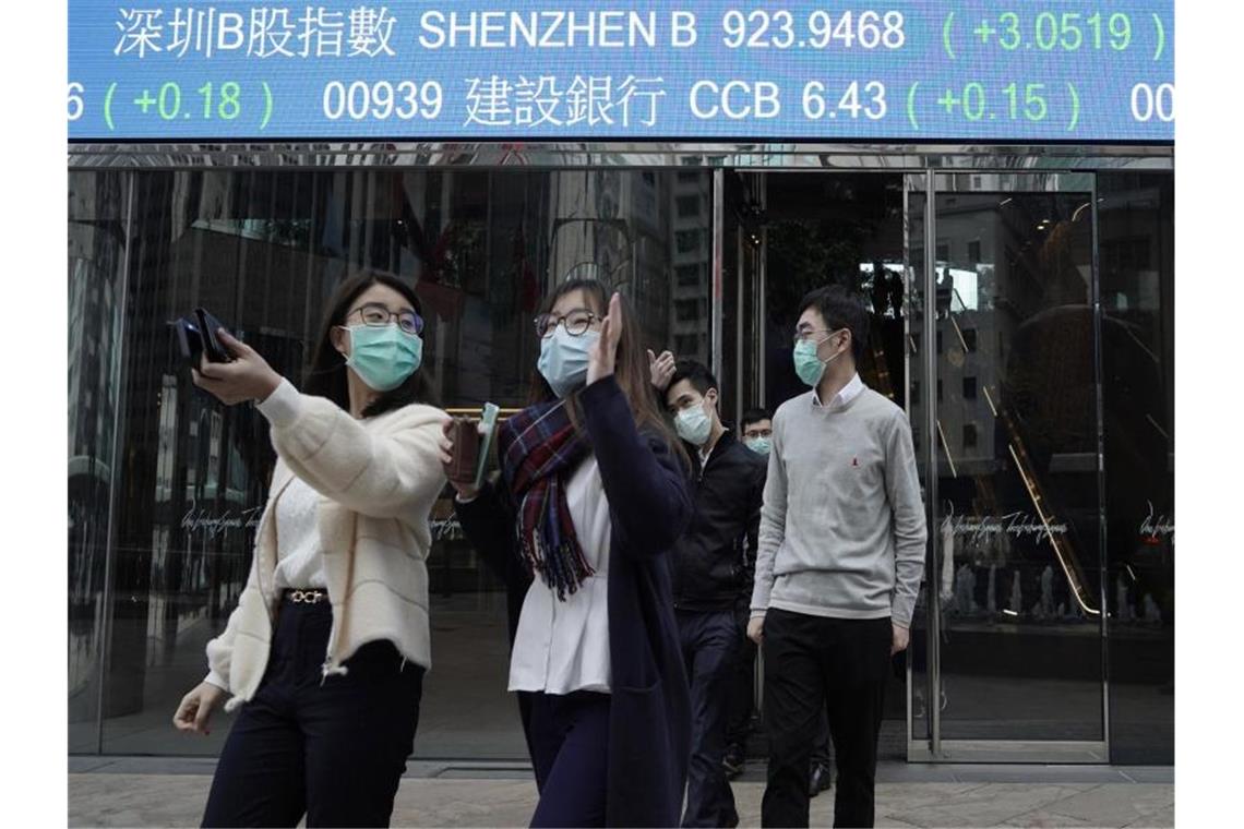 Personen mit Mundschutz gehen über eine Straße in China. Foto: Kin Cheung/AP/dpa/Archivbild