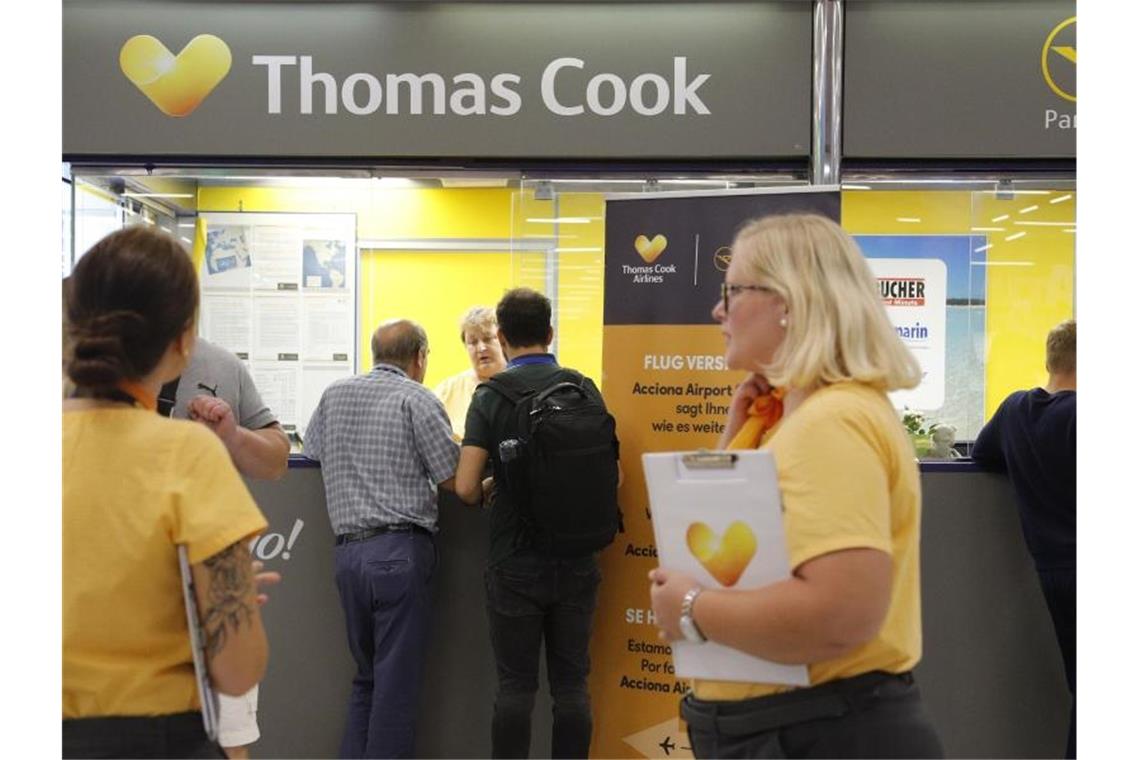 Personen stehen vor dem Büro von Condor und Thomas Cook im Flughafen Palma de Mallorca. Foto: Clara Margais/dpa