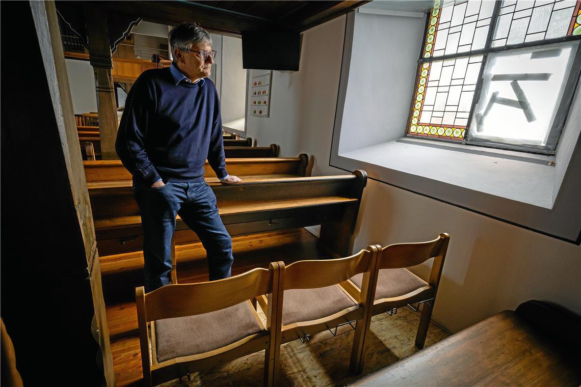 Pfarrer Ulrich Hörrmann vor dem beschädigten Fenster. Drei Stühle ersetzen vorerst die ausgebaute Sitzbank. Foto: Alexander Becher