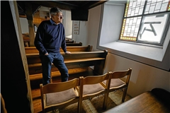 Pfarrer Ulrich Hörrmann vor dem beschädigten Fenster. Drei Stühle ersetzen vorerst die ausgebaute Sitzbank. Foto: Alexander Becher