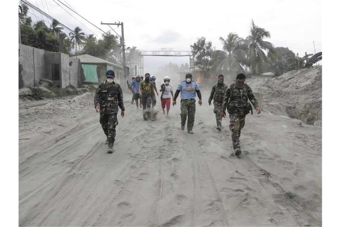 Philippinische Polizisten und Soldaten laufen auf einer mit Vulkanasche bedeckten Straße. Foto: Aaron Favila/AP/dpa