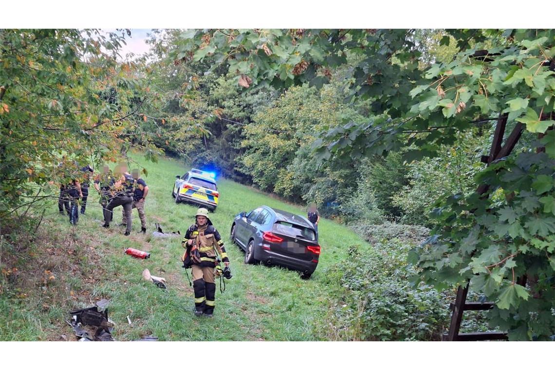 Polizei und Feuerwehr stehen nach einer Verfolgungsjagd neben einem Auto in einem Waldstück. Ein 17-Jähriger hat sich bei Passau in einem gestohlenem Auto eine Verfolgungsjagd mit der Polizei geliefert. Dabei baute er mehrere Unfälle, wie die Polizei mitteilte.