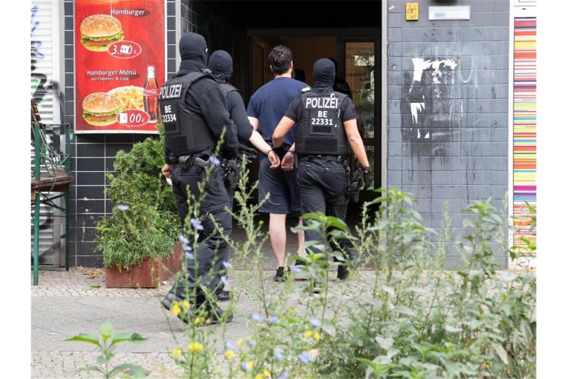 Polizeibeamte führen einen mit Handschellen gefesselten Mann in ein Haus in Berlin-Kreuzberg. Foto: Paul Zinken/dpa