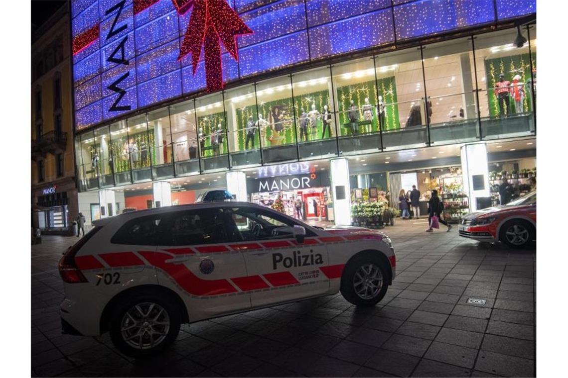 Polizeifahrzeuge stehen vor dem Kaufhaus Manor an der Piazza Dante im schweizerischen Kanton Tessin. Eine Frau hat in dem Warenhaus heute zwei Passantinnen mit einem Messer angegriffen. Foto: Pablo Gianinazzi/KEYSTONE/Ti-Press/dpa