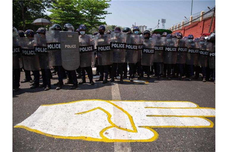 Polizisten blockieren eine Straße, auf die ein Dreifingergruß als Zeichen des Widerstands gezeichnet ist. Foto: Theint Mon Soe/SOPA Images via ZUMA Wire/dpa