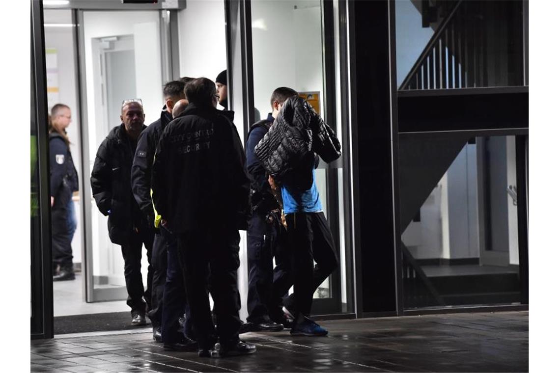Polizisten führen den Tatverdächtigen aus der Schlosspark-Klinik ab. Der Prozess gegen den mutmaßlichen Mörder von Fritz von Weizsäcker hat begonnen. Foto: Paul Zinken/dpa