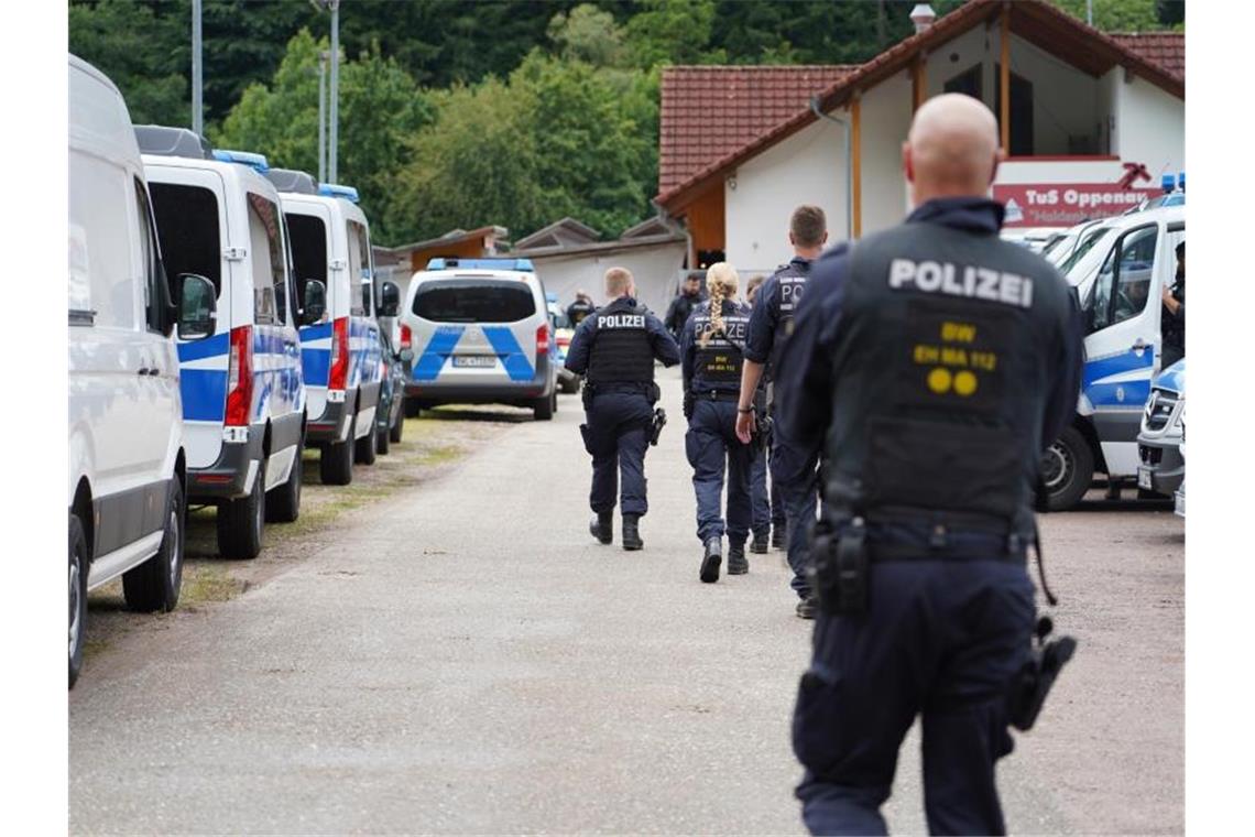 Polizisten gehen an einem Parkplatz in Oppenau an Polizeifahrzeugen vorbei. Foto: Benedikt Spether/dpa