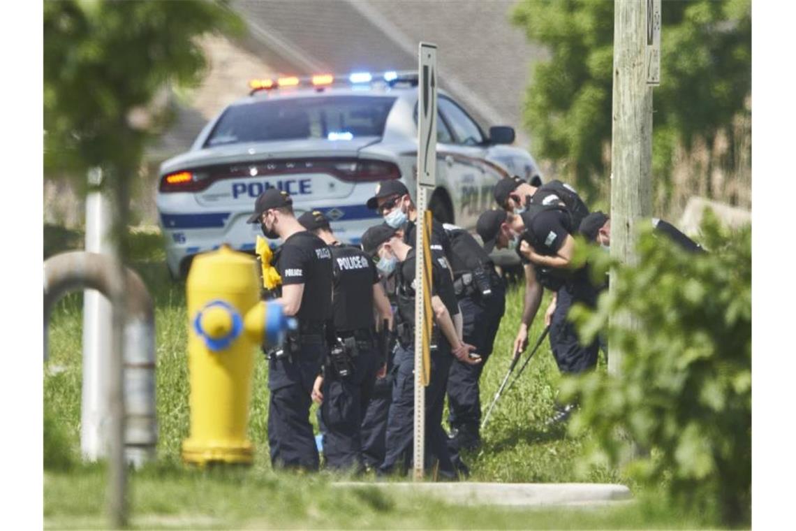 Polizisten in Reihe untersuchen den Tatort eines Autounfalls in London, Ontario. Nach einem Angriff mit einem Auto, bei dem vier Menschen aus einer muslimischen Familie getötet worden sind, geht die Polizei Berichten zufolge von einem rassistischen Tatmotiv aus. Foto: Geoff Robins/The Canadian Press via AP/dpa