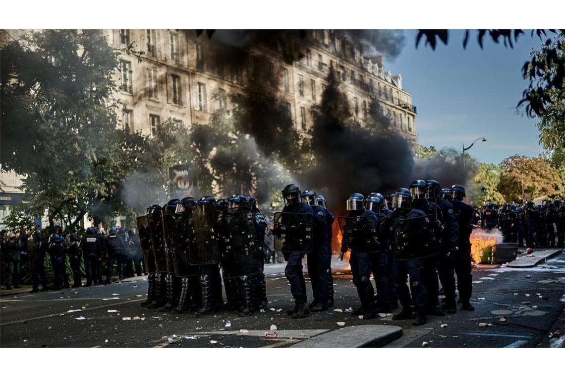 Polizisten stehen bei Protesten gegen unterfinanzierte Schulen in Paris auf der Straße während hinter ihnen Mülltonnen brennen.