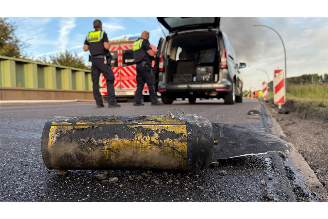 Polizisten stehen hinter einem Metallbehälter. Trümmerteile sollen bei dem Brand Hunderte Meter weit geflogen sein.
