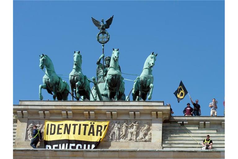 Polizisten stehen neben Aktivisten der „Identitären Bewegung“ auf dem Brandenburger Tor. Sie zeigen ein Transparent mit der Aufschrift „Grenzen schützen - Leben retten“. Foto: Paul Zinken/dpa