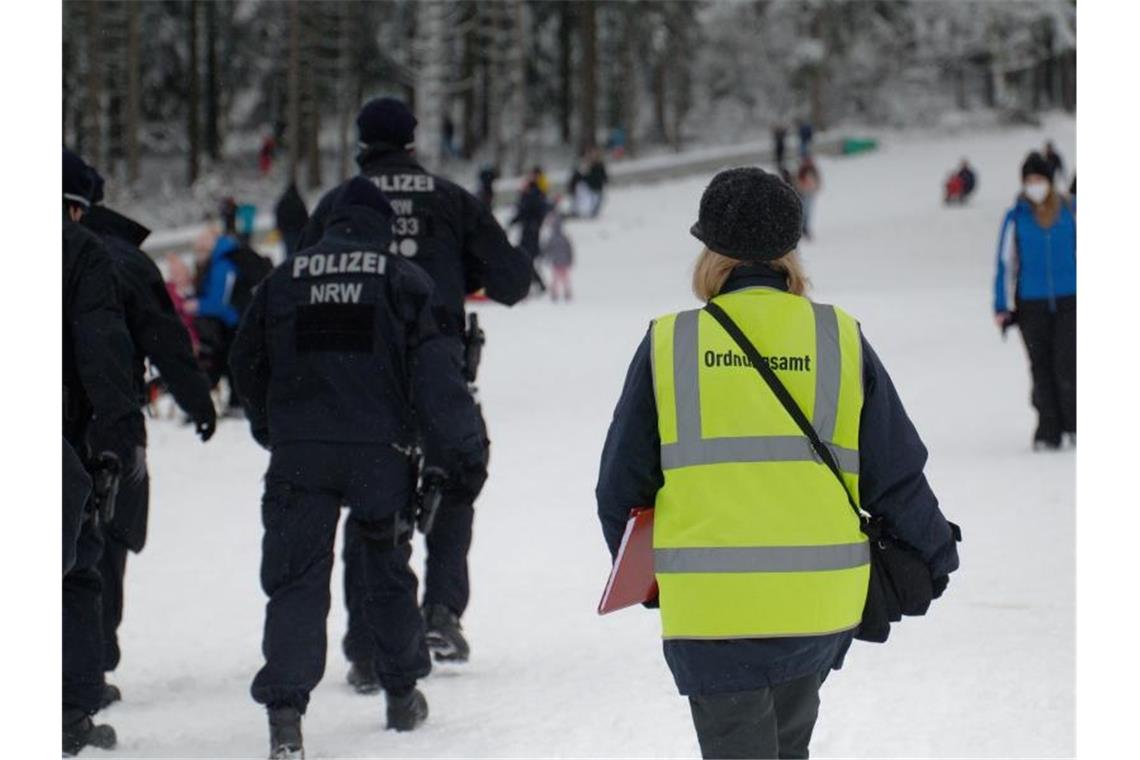 Polizisten und eine Mitarbeiterin des Ordnungsamtes stehen auf einer Piste im Skigebiet in Winterberg. Foto: Henning Kaiser/dpa